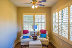 two chairs in a sitting room with a lamp and windows with plantation shutters