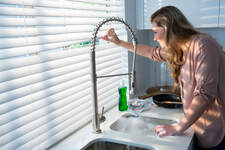 woman standing at kitchen sink looking out horizontal window blinds